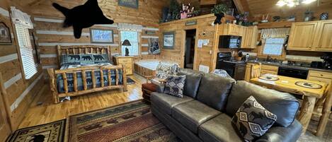 A log cabin interior with a living room, kitchen, and a ceiling fan.