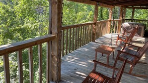 Eine Holzterrasse mit Geländer, Whirlpool und einer Schaukelstuhlsitzgelegenheit.
