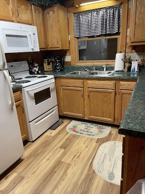 Une cuisine avec des meubles en bois, une cuisinière blanche, un four à micro-ondes, un évier et une fenêtre ornée de rideaux à carreaux.