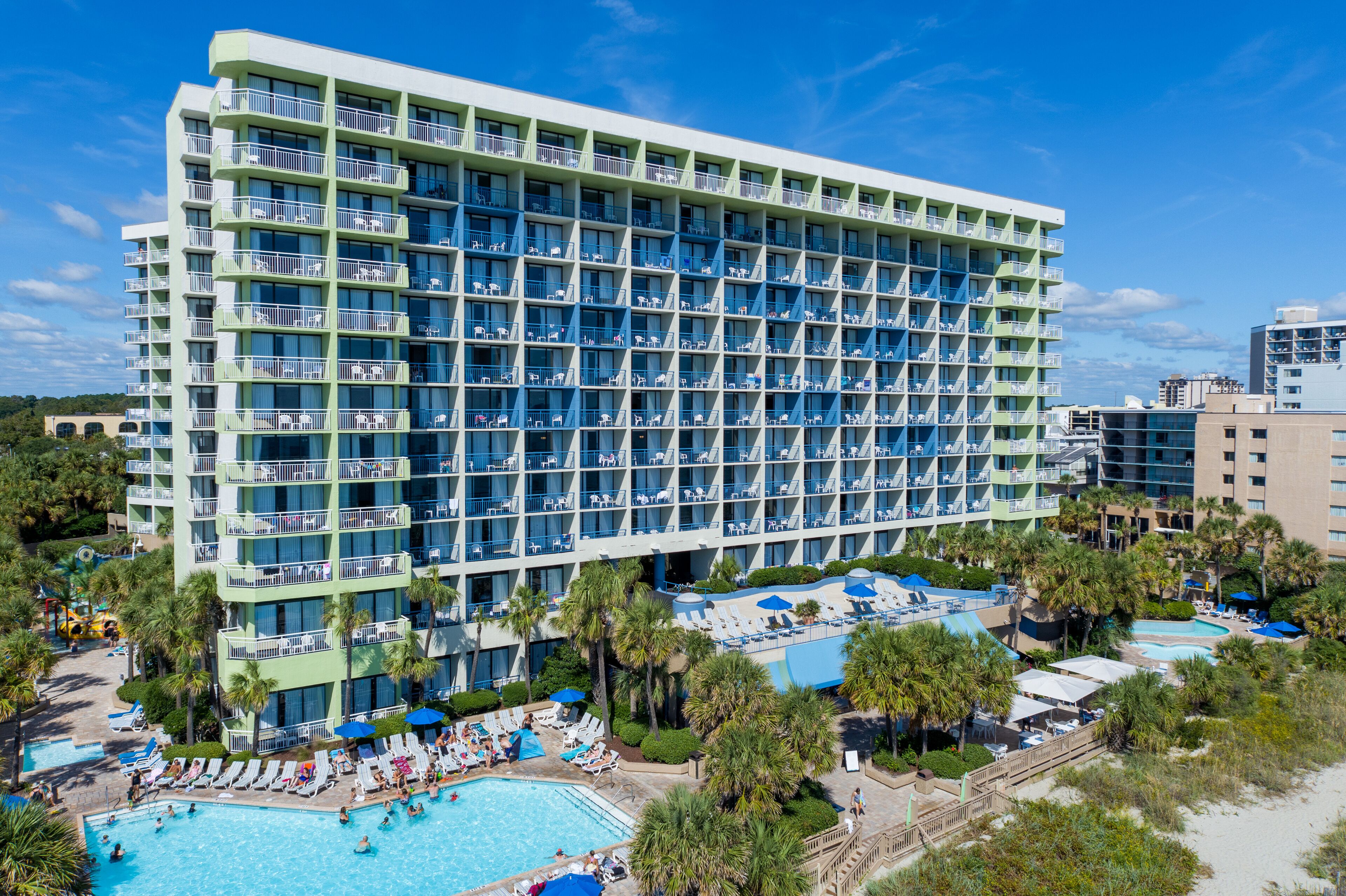 A multi-story hotel with balconies, a swimming pool, and a beach area.