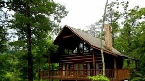 Un chalet rustique doté d’une terrasse en bois, entouré d’une forêt dense.