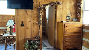 Un intérieur en bois avec un téléviseur fixé au mur, une commode en bois et une petite table avec une lampe.