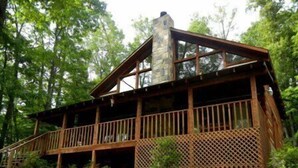 A cabin with a wooden deck, a stone chimney, and a lattice fence.