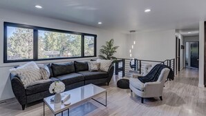 A modern living room with a sofa, armchair, coffee table, and large windows. - Modern home with privacy of the hills right in town! (Rapid City)