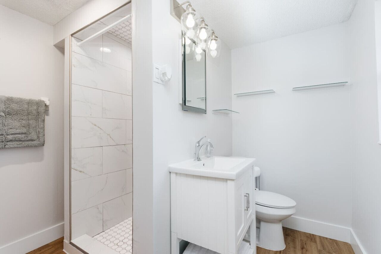 Een moderne badkamer met een douchecabine van glas, een wit wastafelmeubel met spiegel en een toilet.
