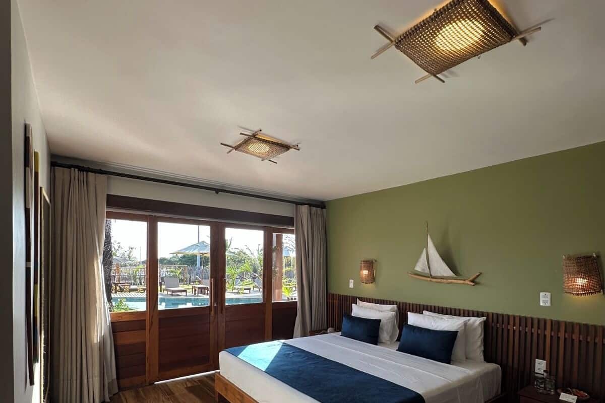 Um quarto espaçoso com uma cama grande, piso de madeira, vista para uma piscina e duas ventoinhas de teto.
