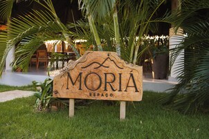 A wooden sign with the name 'MORIA ESPAÇO' in a tropical setting with palm trees.