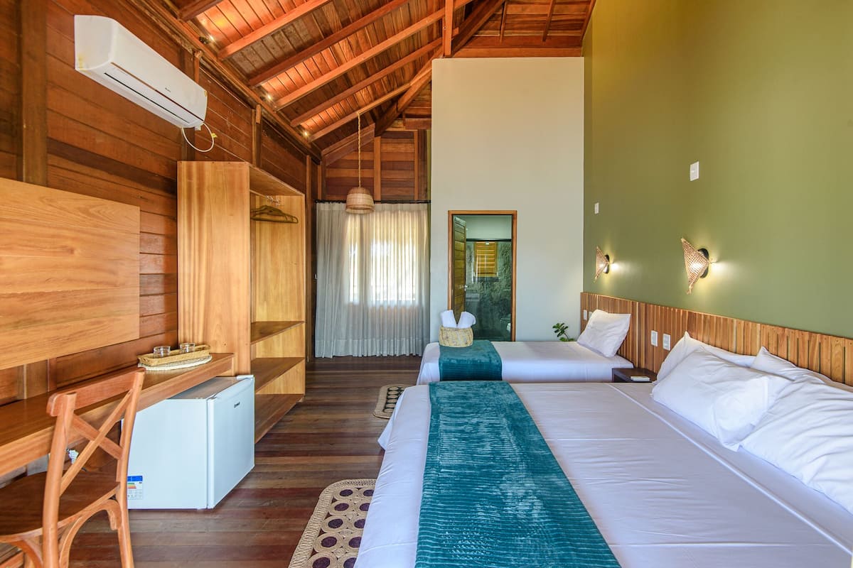 Quarto estilo cabana de madeira com duas camas, um pequeno frigorífico e uma escrivaninha de madeira.