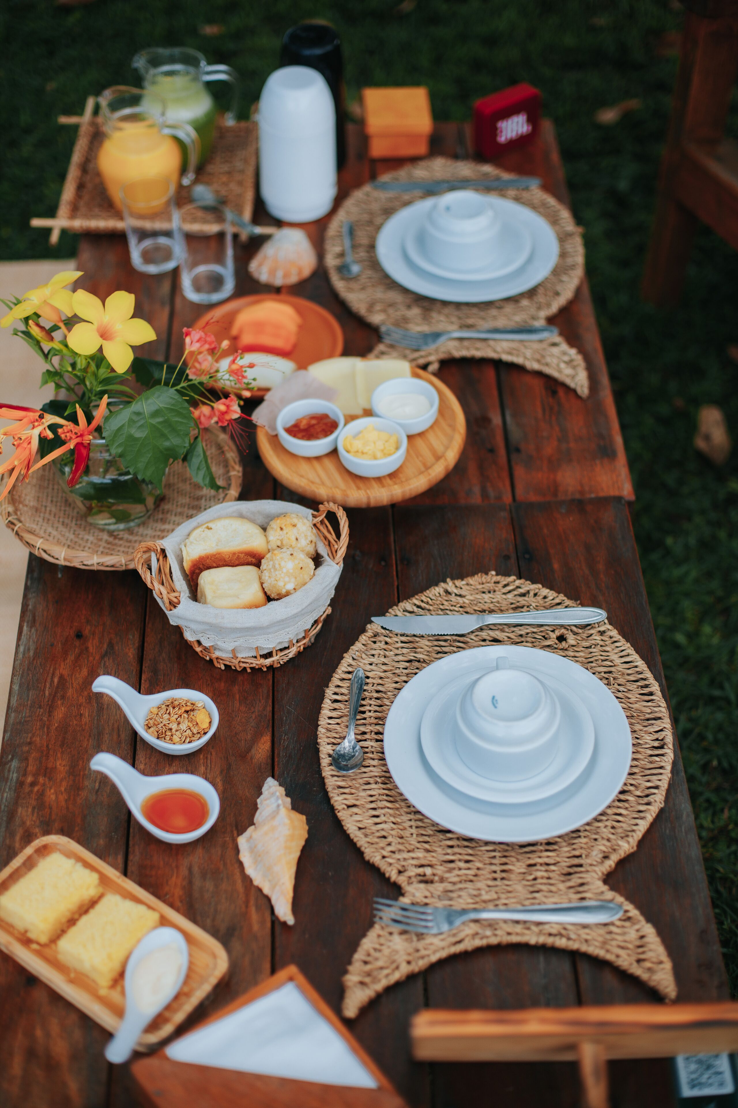 A wooden table set for breakfast with various dishes, drinks, and utensils.