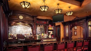 A bar area with wooden bar counters, red upholstered bar stools, and ornate chandeliers. - Irish Cottage Inn & Suites (Galena)