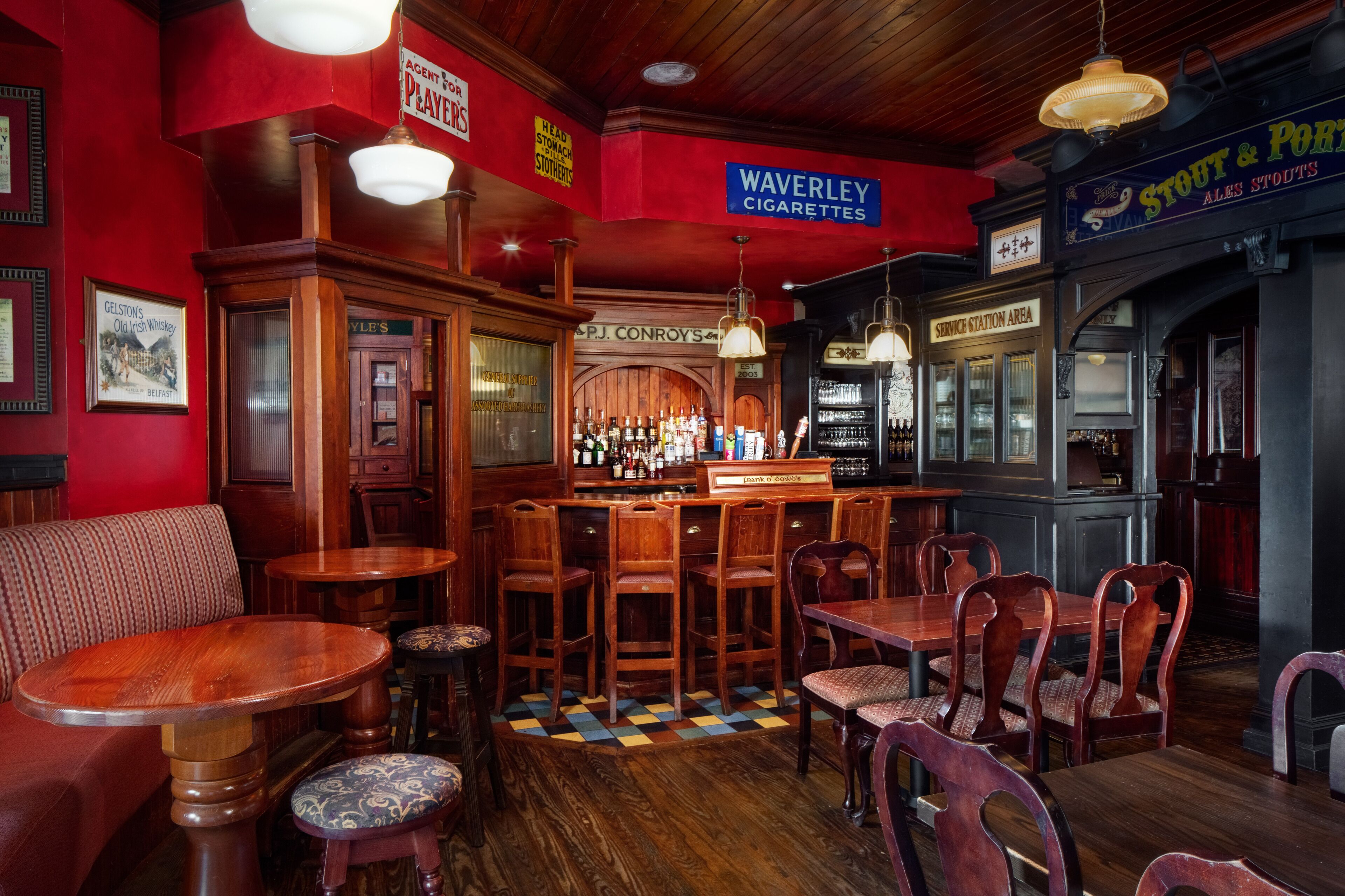 A bar area with wooden furniture, a bar counter, and various signs including one for Waverley Cigarettes.