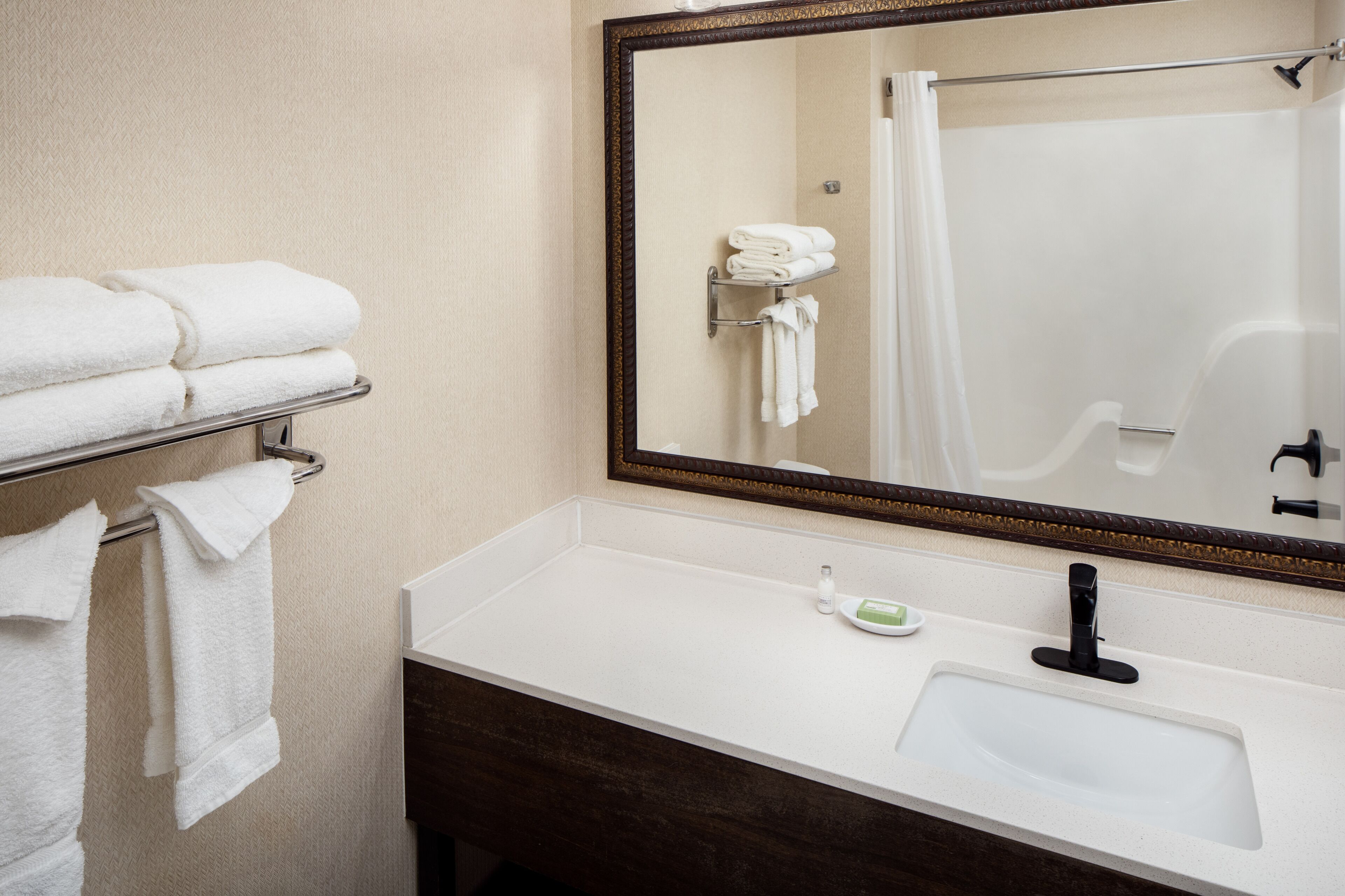 A bathroom with a white sink, a mirror, and a towel rack with folded towels.