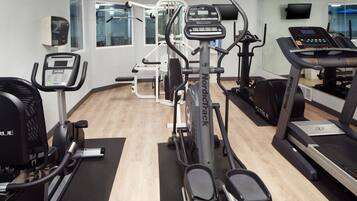 Een sportschool met cardioapparatuur, krachtapparaten en een spiegelwand.