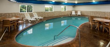 Una piscina interior con agua cristalina, rodeada de sillones de descanso y una mesa.