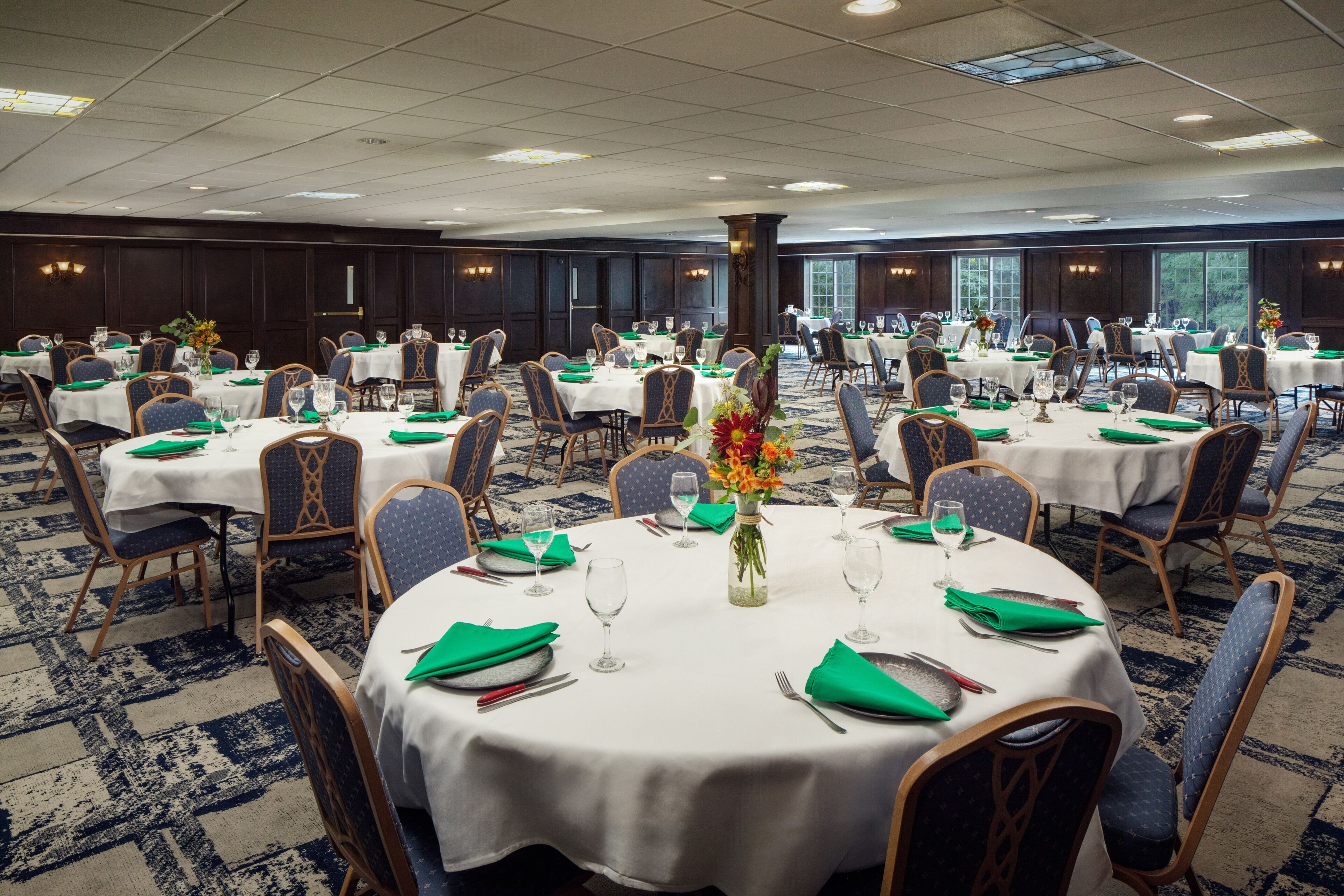 A banquet hall with round tables, chairs, and green napkins.