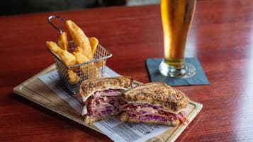Ein halbiertes Sandwich, ein Glas Bier und eine Korb Pommes auf einem Holztisch.