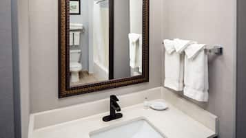 A bathroom with a white sink, a large mirror, and a towel rack with several white towels.