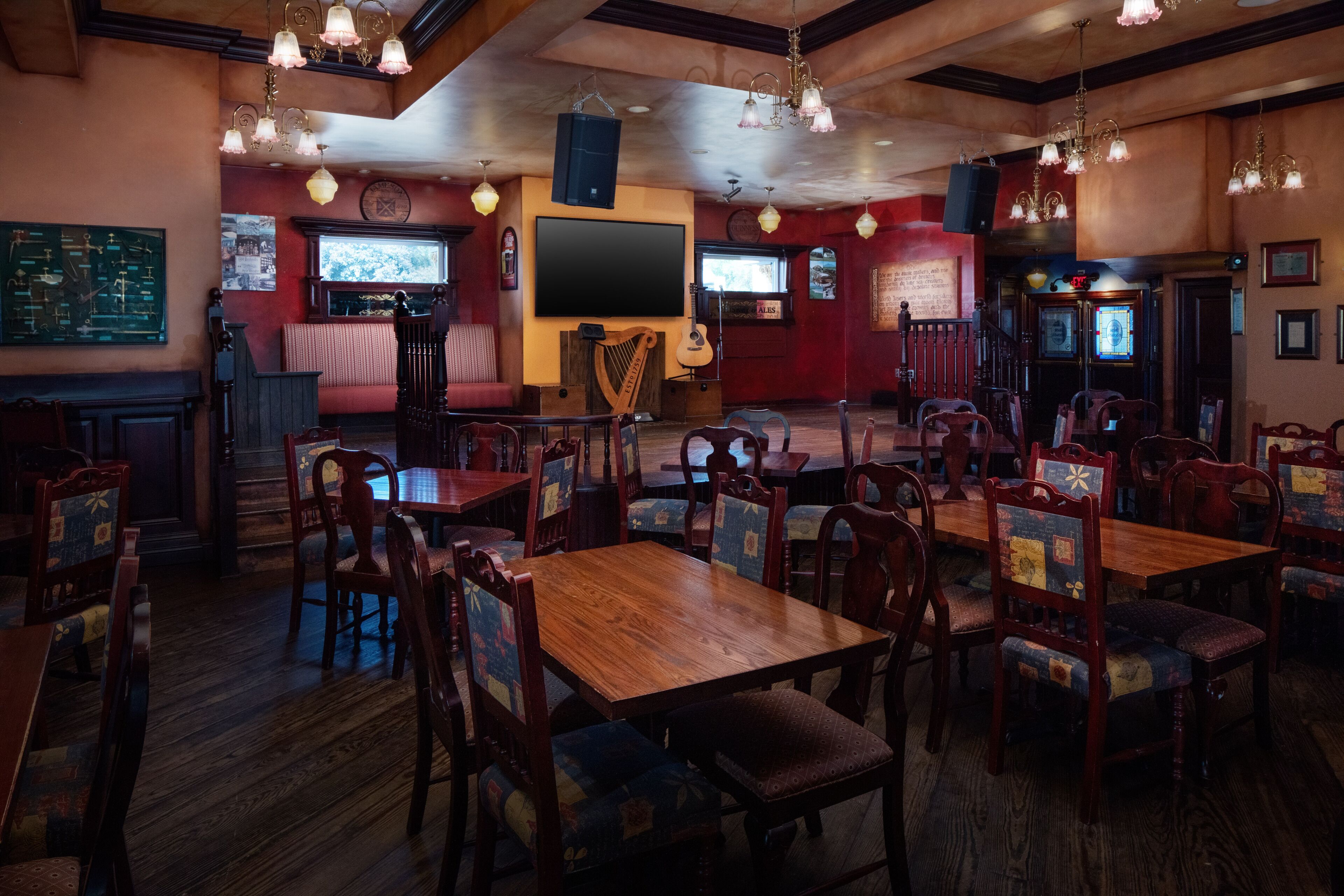 Um restaurante com mesas e cadeiras de madeira, um palco com instrumentos musicais e uma tela grande.