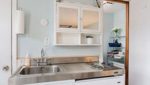 Une cuisine avec un évier en acier inoxydable, un meuble blanc aux portes en verre et un plan de travail sur lequel se trouvent une bouilloire et une petite plante.
