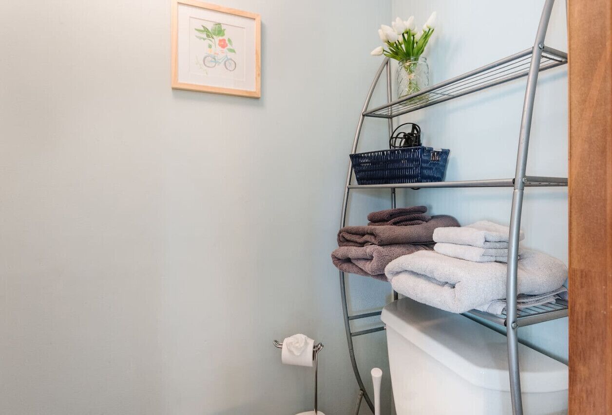 Un baño con un estante metálico que sostiene toallas y un cuadro en la pared.