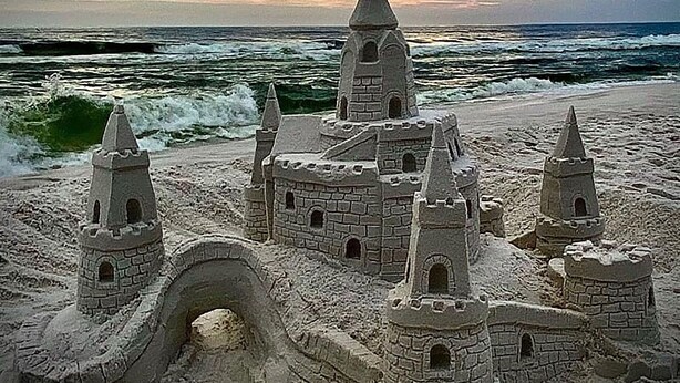 A sandcastle with multiple towers and a moat, located on a beach with the ocean in the background. - Beach Service|Gulf Front|Private Balcony|PCB|CC514 (Panama City Beach)