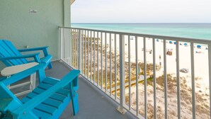 A balcony with blue chairs, a white railing, and a view of a beach with umbrellas and people. - Beach Service|Gulf Front|Private Balcony|PCB|CC514 (Panama City Beach)