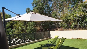 Eine Terrasse mit Kunstgrras, einer Holzterrasse und zwei gelben Liegestühlen unter einem großen Sonnenschirm.