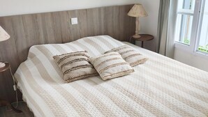A neatly made bed with a striped quilt, a wooden headboard, and a bedside lamp. There are three framed pictures on the wall above the bed. - Maison Dans Résidence Avec Piscine "jetez L'ancre" (La Flotte)