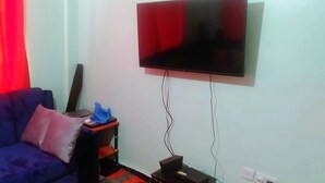 Ein Wohnzimmer mit einem blauen Sofa, einem an der Wand montierten Flachbildfernseher und einem kleinen Tisch mit einer Kiste und einem blauen Stoff.