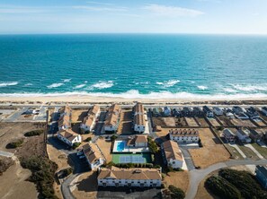 An aerial view of a coastal residential area with houses, a tennis court, and a beach.