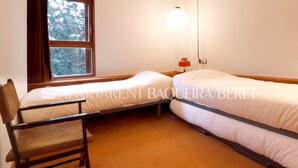 Ein Zimmer mit zwei Einzelbetten, einem Holzstuhl, einem Fenster mit Vorhängen und einer Pendelleuchte.