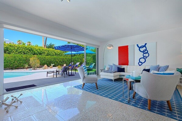 Una sala de estar moderna con vista a la piscina, un sofá blanco y un tapete de diseño azul y blanco.