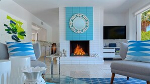 Una sala de estar moderna con chimenea, televisor y comedor con mesa de vidrio.