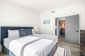 A bedroom with a large bed, a nightstand, a dresser, and a door leading to a bathroom.