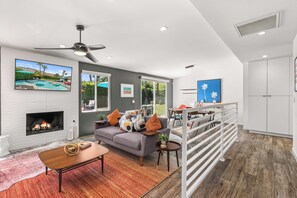 A modern living room with a fireplace, a grey sofa, and a dining area with a view of the outdoors.