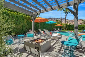 A covered outdoor area with lounge chairs, umbrellas, and a fire pit.