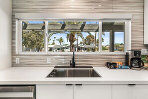A kitchen with a large window, a stainless steel sink, and a coffee maker on the counter.