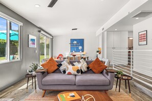 A modern living room with a grey sofa, a coffee table, and a dining area in the background.