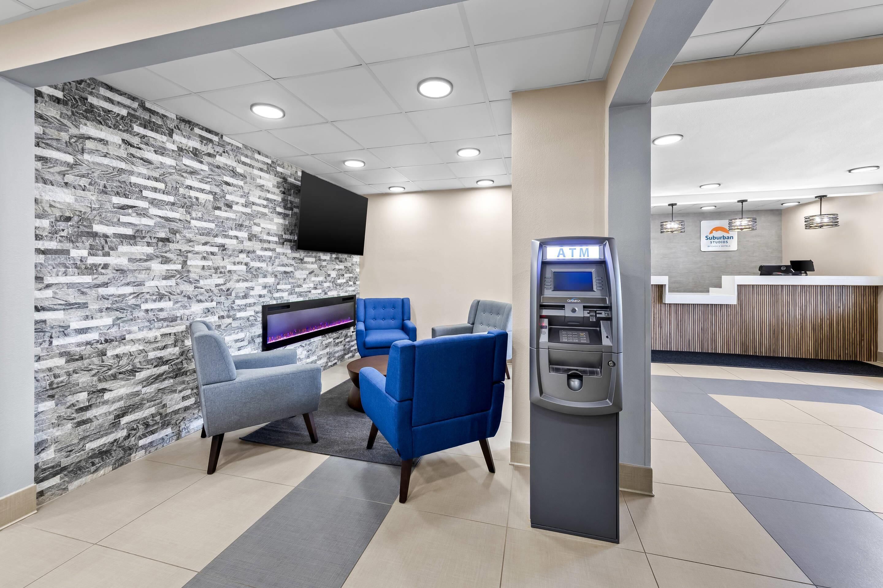A hotel lobby with a marble wall, seating area, and an ATM.