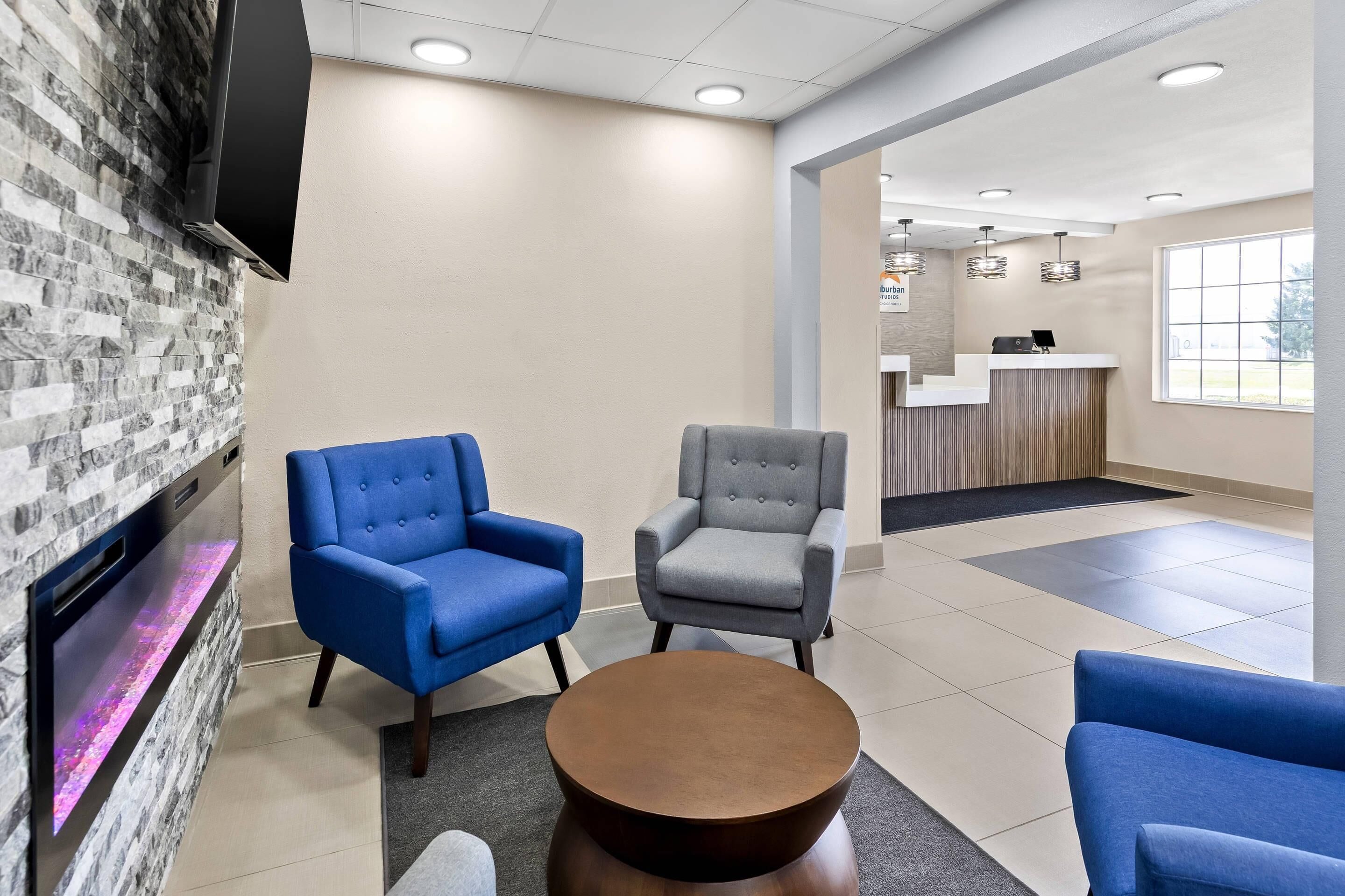 Un hall d’entrée comprenant deux fauteuils, une table basse, un comptoir d’accueil et un téléviseur fixé à un mur en pierre.