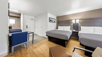 A hotel room with two beds, a desk, a chair, and a small table.