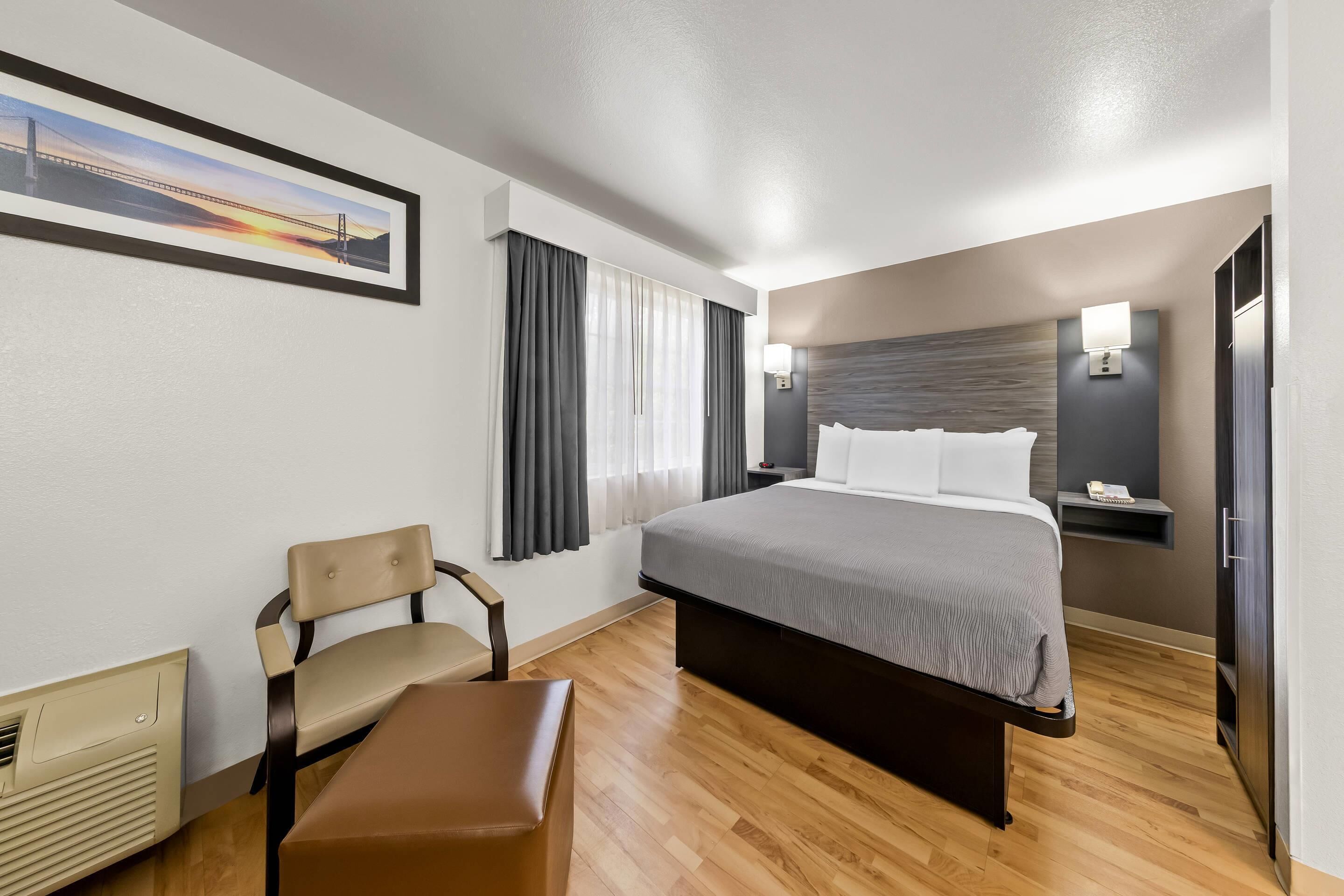 A hotel room with a bed, a chair, a desk, and a nightstand.
