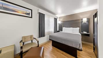 A hotel room with a bed, a chair, a desk, and a nightstand.