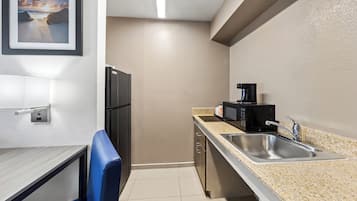 A compact kitchen with a refrigerator, microwave, sink, and a blue chair.