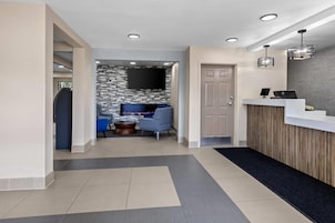 A hotel reception area with a reception desk, a seating area with a TV, and a hallway leading to a door.