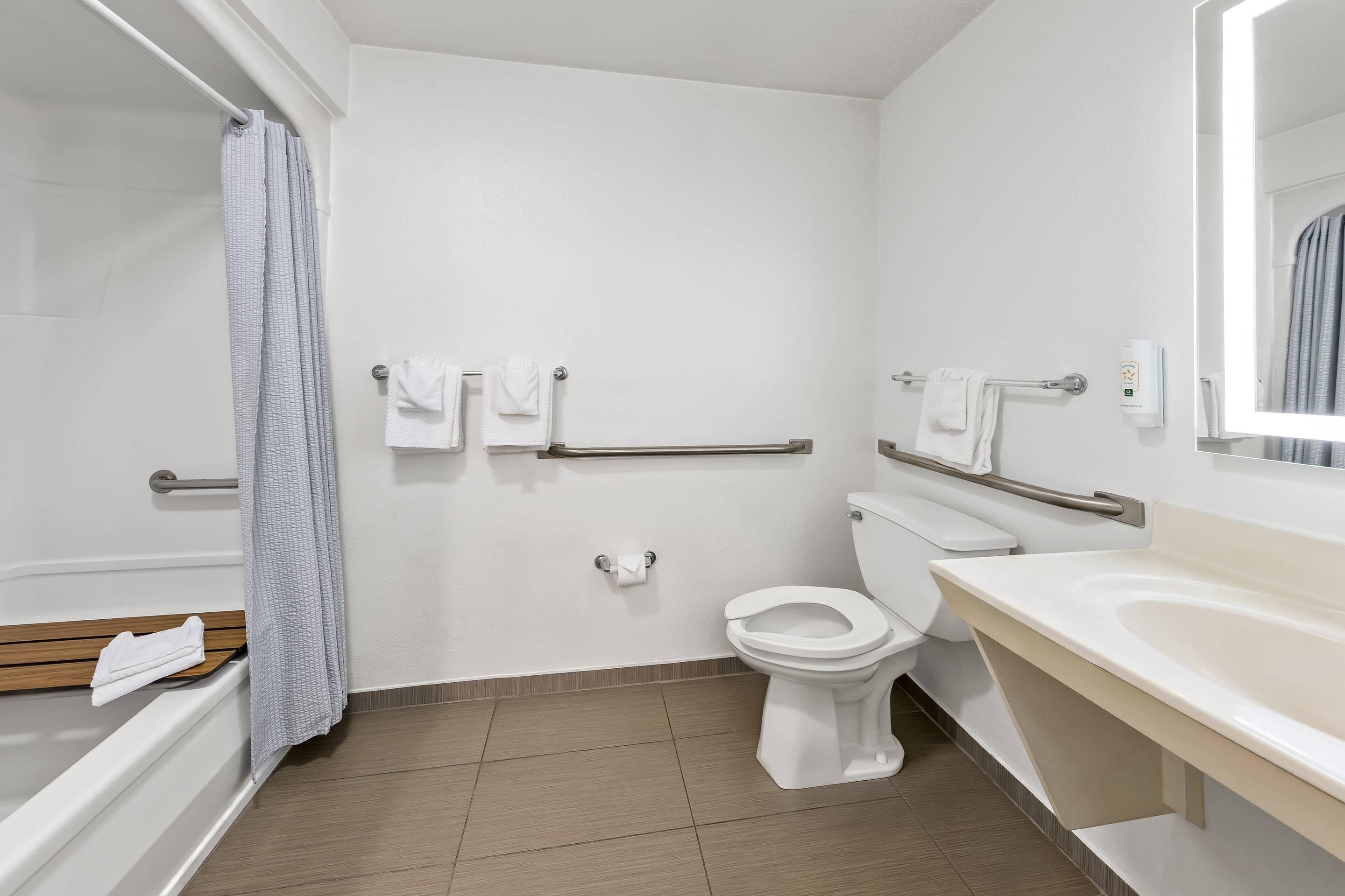 A bathroom with a toilet, a sink, a bathtub, and a shower. There are grab bars installed near the toilet and the shower.