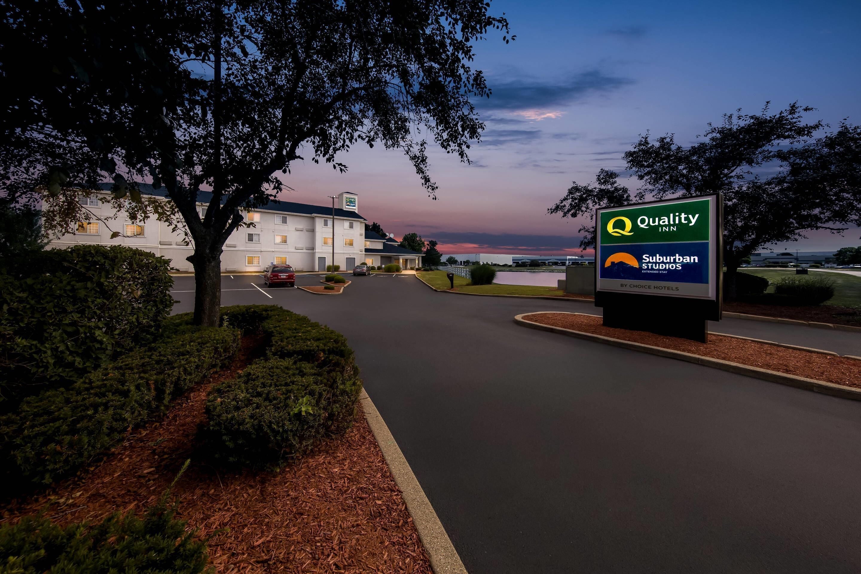 A hotel sign with 'Quality Inn' and 'Suburban Studios' branding, a parking lot, and a building with multiple windows.