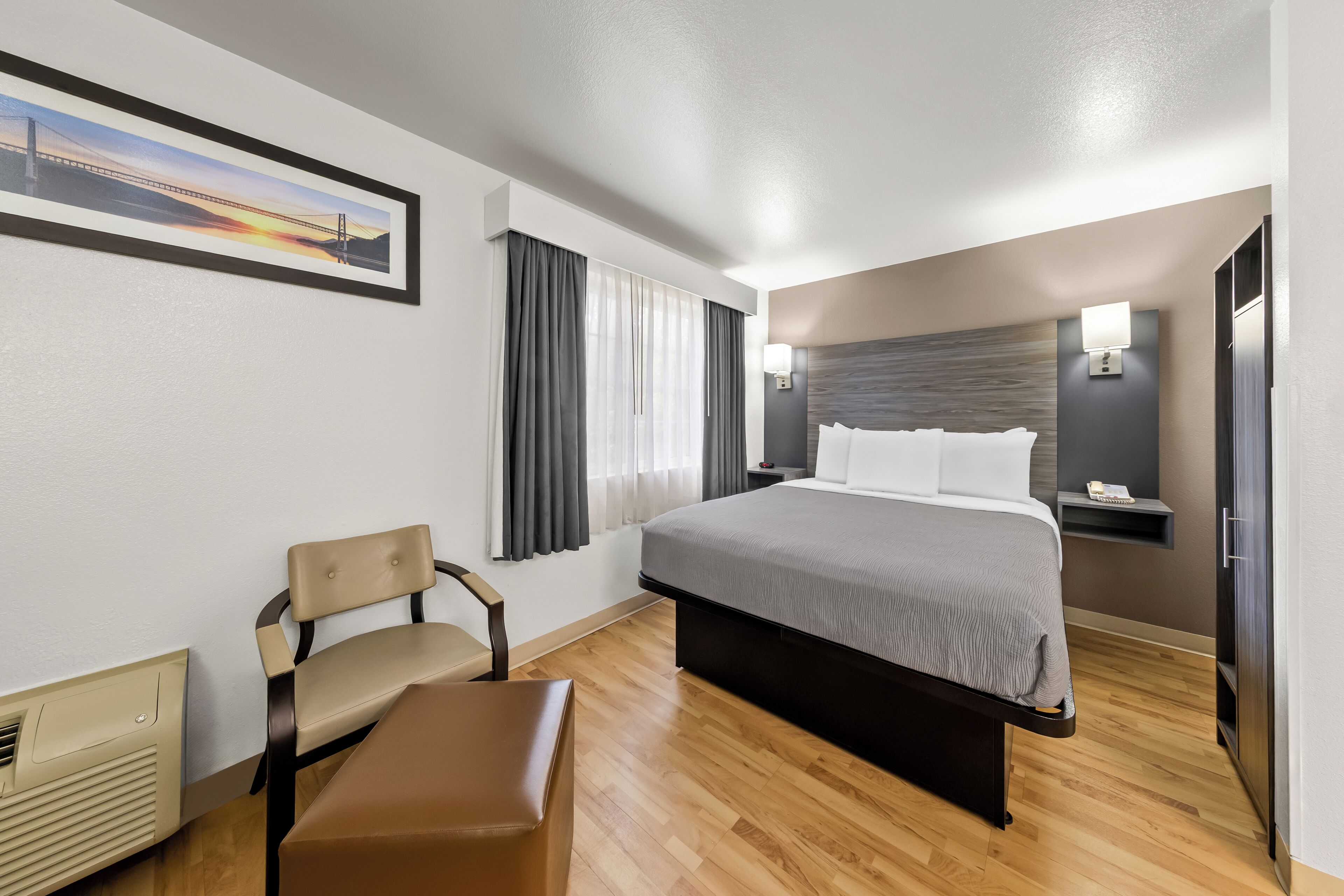 Una habitación de hotel con cama, una silla, un escritorio y un cuadro en la pared.