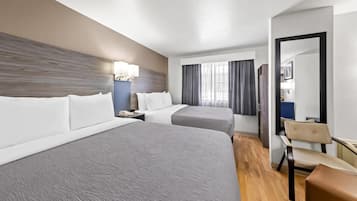 Une chambre d’hôtel avec deux lits, un bureau, une chaise, un miroir et une fenêtre avec des rideaux.