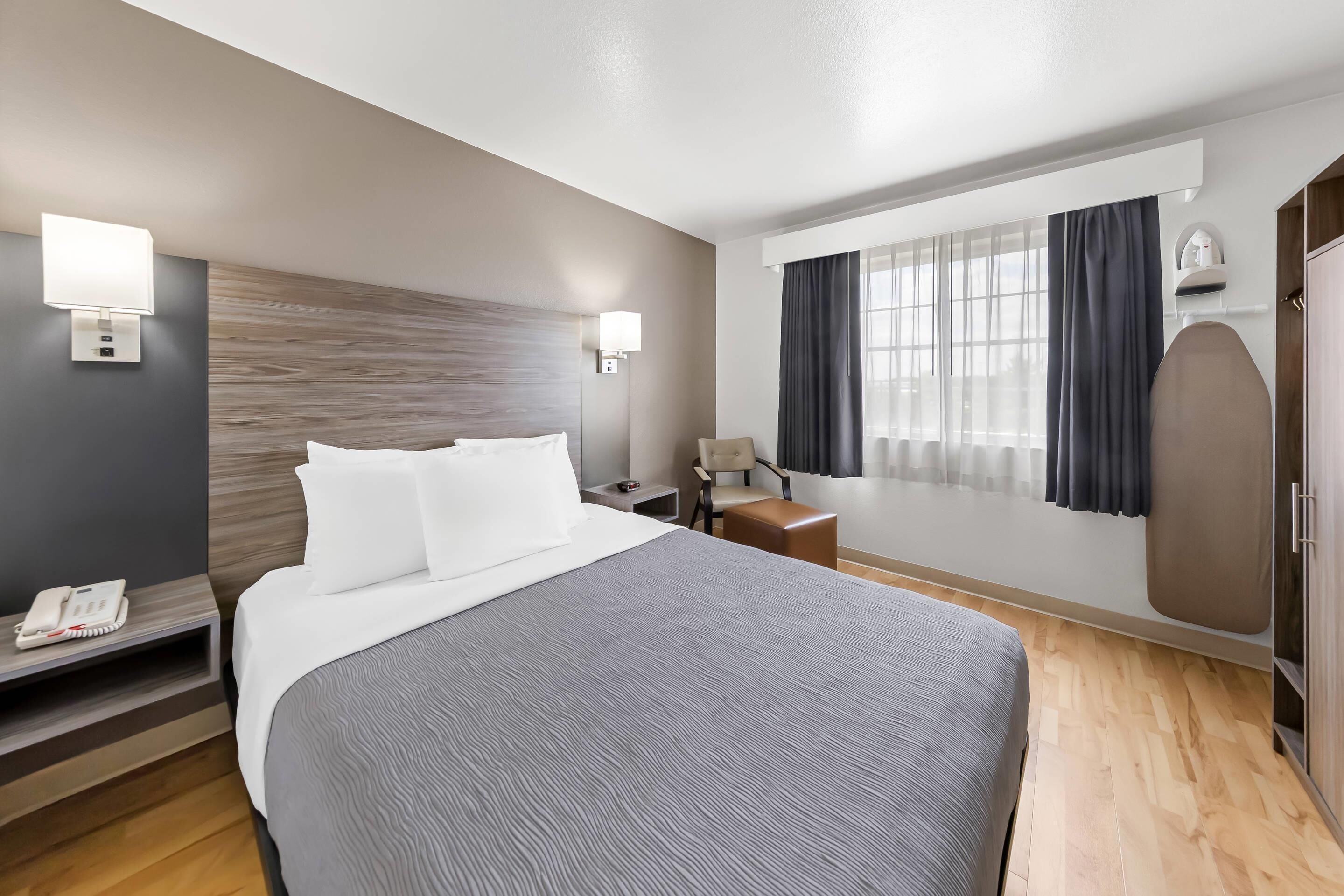A hotel room with a large bed, bedside tables, a desk, a chair, a wardrobe, and a window with curtains.